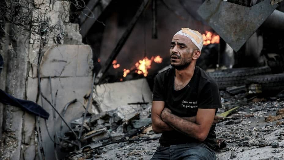 An injured man sits in front of a smouldering building in the aftermath of an Israeli strike on Gaza City on October 26, 2023, as battles continue between Israel and the Palestinian Hamas group. (Photo by Omar El-Qattaa / AFP) (Photo by OMAR EL-QATTAA/AFP via Getty Images)